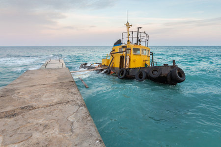 Abandoned Tugboat moored to a pier in the sea at sunsetの写真素材