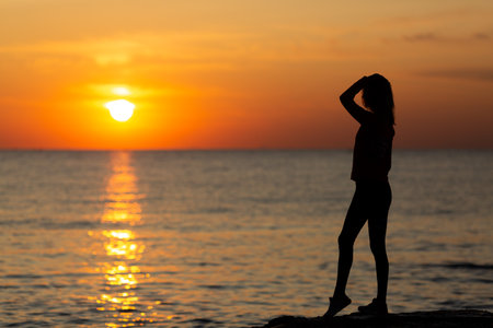 Silhouette of a young woman standing on the beach at sunset.の写真素材