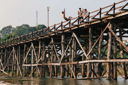 Kanchanaburi, Thailand - December 09, 2013: A child jumping from Saphan Mon (Mon Bridge) to Song Karia river with tourists taking photograph from the wooden bridgeのeditorial素材