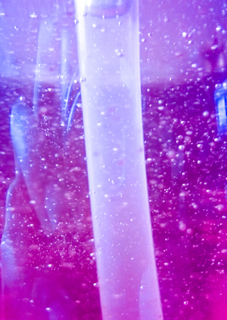 Abstract background with air bubbles within purple-orange dish soap liquid with plastic tubeの写真素材
