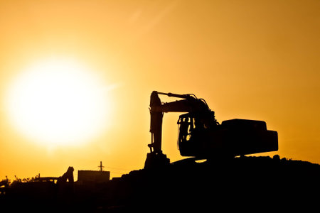 Silhouette of digger before giant sun on construction site with working manの写真素材
