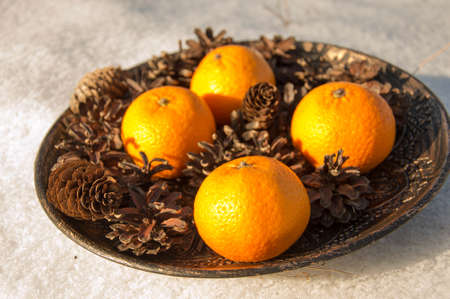 Tangerines in a wooden plate with pine cones on a white backgroundの写真素材