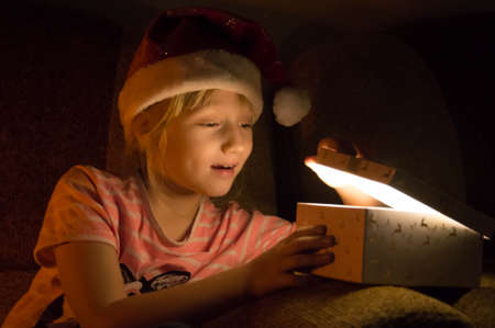 Little girl in santa hat opening christmas gift box at nightの写真素材