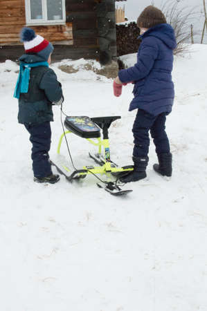 Children play on the snow in the winter. A boy and a girl with a snowmobile.の写真素材