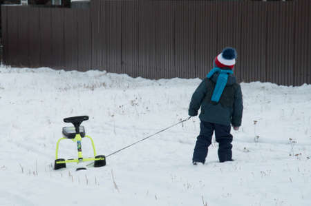 A little boy in a winter hat walks through the snow on a leash.の写真素材