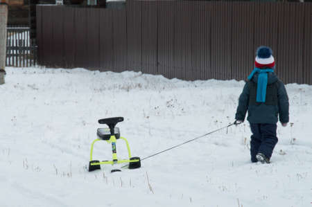 A boy in a winter jacket walks with a snow scooter.の写真素材