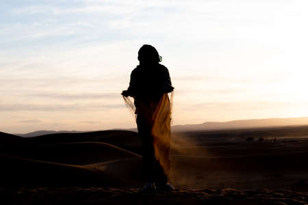 Silhouette of person jumping and throwing sand in the Sahara against a sunsetの写真素材