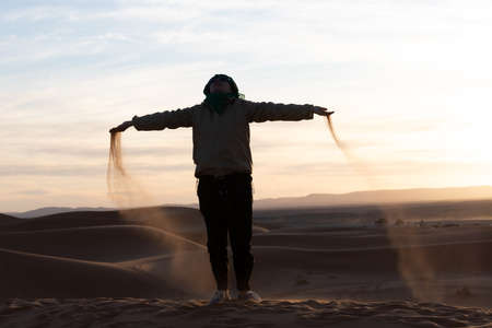 Silhouette of person jumping and throwing sand in the Sahara against a sunsetの写真素材