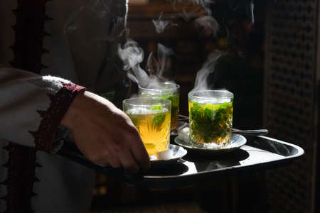 Traditional mint tea in glasses steaming backlit by sun being served on trayの写真素材