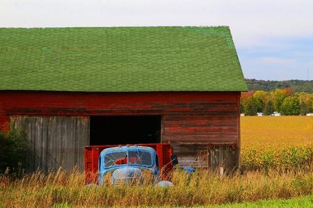 Run down blue truck parked in front of an old red barn in the countryの写真素材