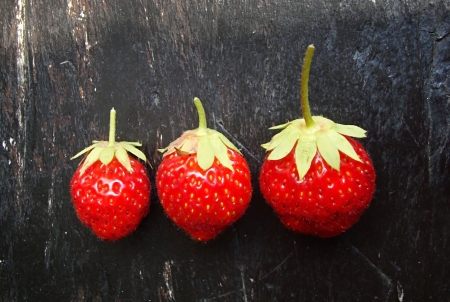 three ripe, red strawberries on a wooden backgroundの写真素材