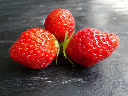 three ripe, red strawberries on a wooden backgroundの写真素材
