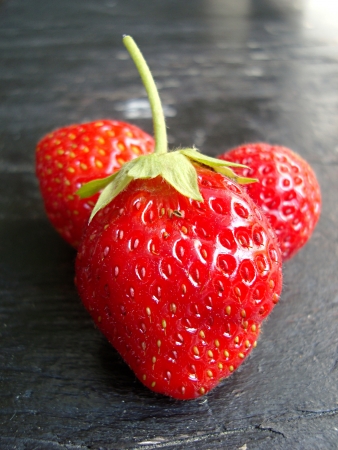 three ripe, red strawberries on a wooden backgroundの写真素材