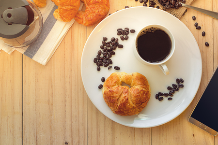 The Concept morning Breakfast, Flatlay above view of a cup of hot coffee with Smart phone and Croissant on wooden background.の写真素材