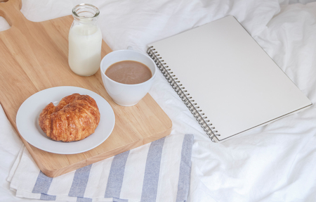 Bed breakfast with coffee cup, croissants and milk in bed, cozy relaxing morning coffee, notebook planner concept の写真素材