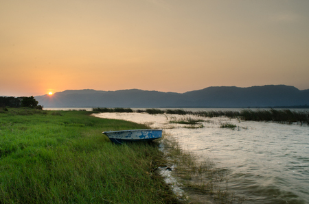 Scenic view of Sunset with boat, mountain, grass and lake waterの写真素材