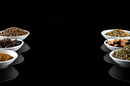 Mix Spice anise aniseed cinnamon fenugreek creating frame with space for text in white bowl over black backgroundの写真素材