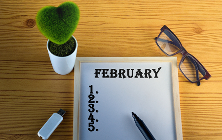 FEBRUARY Business concept - Office desk with White board, pendrive, glasses, pen, and table flowerの写真素材