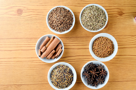 Mixed spice anise, aniseed, cinnamon, fenugreek in bowl over wooden background creating frame with...