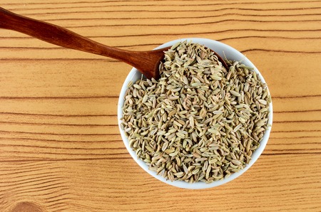 Aniseed  Spice in white bowl with wooden spoon over wooden backgroundの写真素材