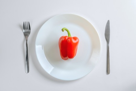 Knife, fork and red pepper, paprica on a white plate on a white background, top viewの写真素材
