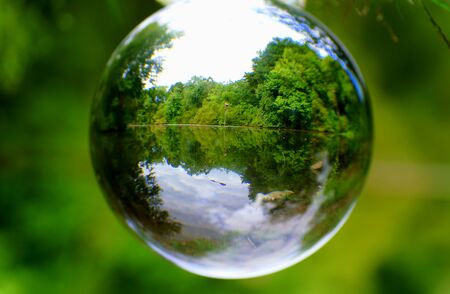 The green forest by a lake captured through a crystal lens ball