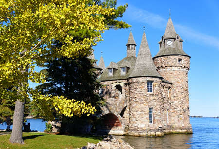 Alexandria Bay, New York, U.S.A - October 24, 2019 - The view of The Power House and Clock Tower of Boldt Castle surrounded by fall foliage along St Lawrence Riverのeditorial素材