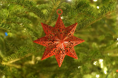 A red star ornament on a lit up Christmas tree