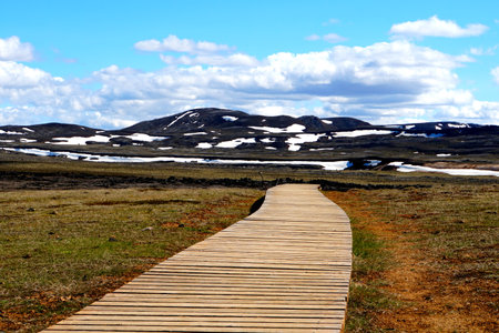 The view of the wooden trail overlooking the partially snowy mountain near Krafla Lava Field, Myvatn, Iceland during the summerの写真素材