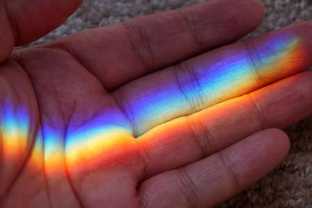 Close up of a palm with rainbow reflection from a glass mirror