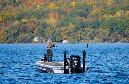 Cayuga Lake, New York, U.S.A - October 15, 2022 - A fisherman on the boat with the background of fall foliageのeditorial素材