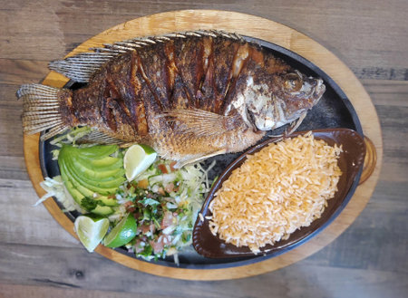 Pescado Frito, a Mexican dish with fried tilapia, yellow rice, salad with a side of salsa and avocado slicesの写真素材