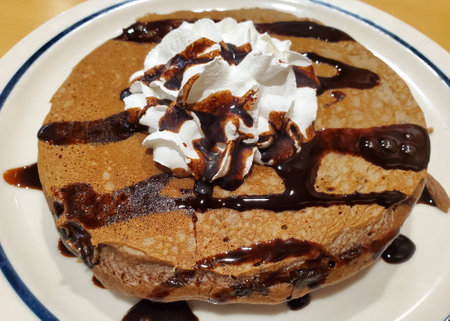 Chocolate chip cookie dough pancake with white cream and syrup on a white plate