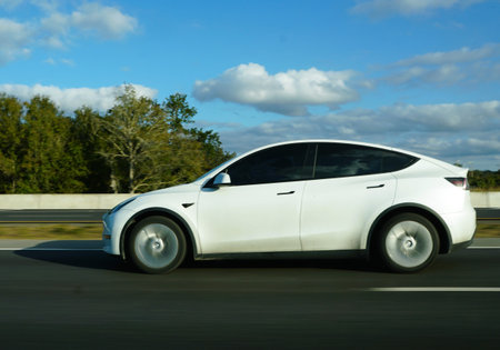 Sarasota, Florida, U.S.A - Jan 4, 2026 - A white Tesla Model Y travels along a highway, showcasing its sleek aerodynamic profile against a backdrop of treesのeditorial素材