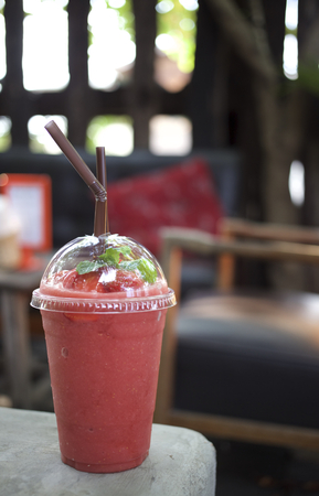 strawberry smoothie in a glass with frozen strawberry and mint leaf on topの写真素材