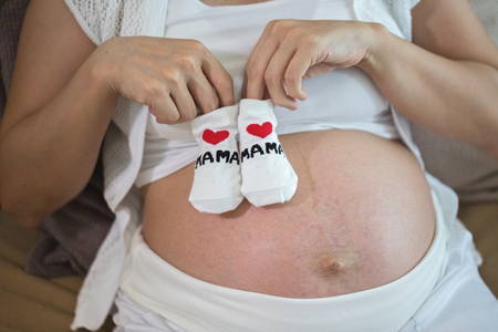 Pregnant woman holding a beautiful baby shoes.の写真素材