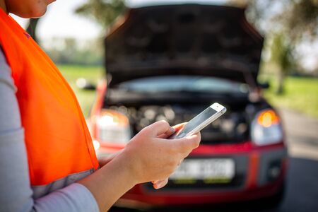 Annoyed young woman in a road distress situation - setting up a warning triangle and calling for...
