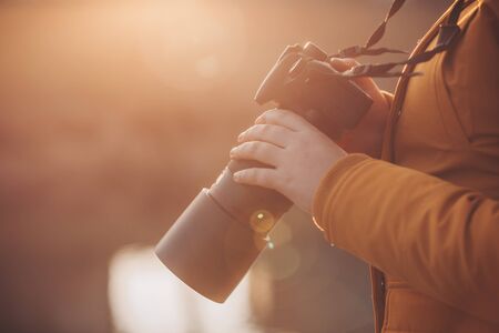 Young woman, photographer holding professional camer in hands during lovely sunsetの写真素材