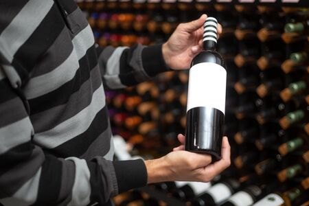 Close up of man hands holding very rare, red cork wine in the huge wine bar, wine degustation, drink...