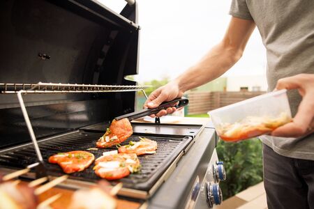 Young man hands turning the meat by fork on the gas grill, food concept