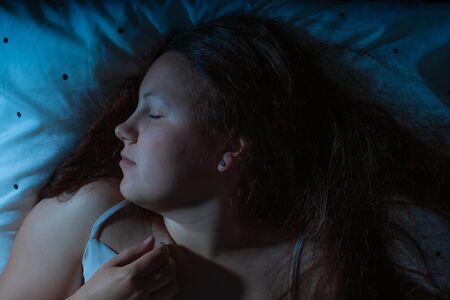 Top view of young woman sleeping cozily on a bed at night, blue nightly coloursの写真素材