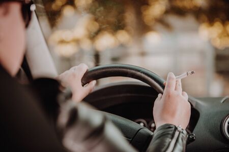 Close up of woman hand smoking cigarette inside the car while driving vehicleの写真素材