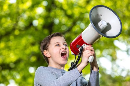 Announcing concept, boy shouting or screaming through the megaphone over forest background with copyspaceの写真素材