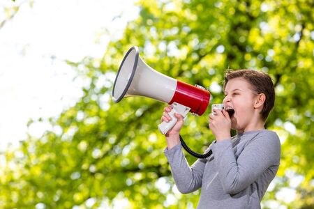 Announcing concept, boy shouting or screaming through the megaphone over forest background with copyspaceの写真素材