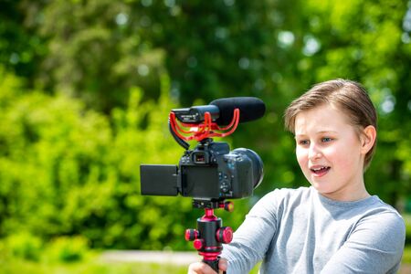 Blogging and vlogging concept, happy smiling boy or blogger with camera recording video blog in outside forestの写真素材