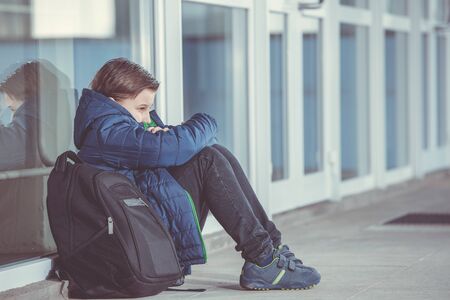 Little boy or child sitting alone on floor in front of the school after suffering an act of bullyingの写真素材