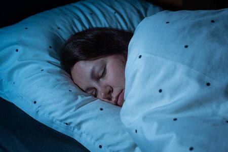 Top view of young woman sleeping cozily on a bed at night, blue nightly colours