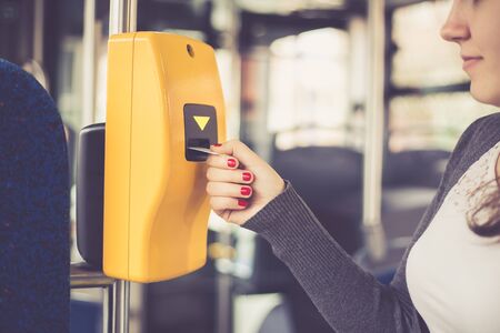 Young woman hand inserts the bus ticket into the validator, validating and ticking, public...