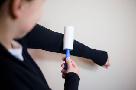 Pretty young brunette woman using roller for her black jumper, using roller for capture of...