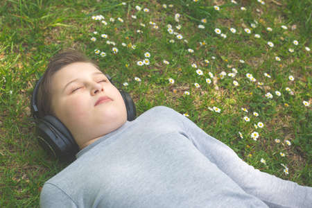 Young boy listening or enjoying a music outside or park with huge headphones, lifestyle concept